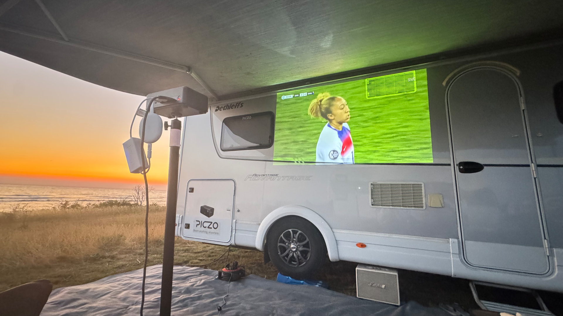 Portabel projektor för husbil och camping – storbild under markisen i solnedgången
